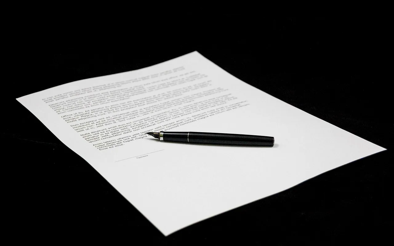 A printed agreement on a dark table, with a pen lying across the page.