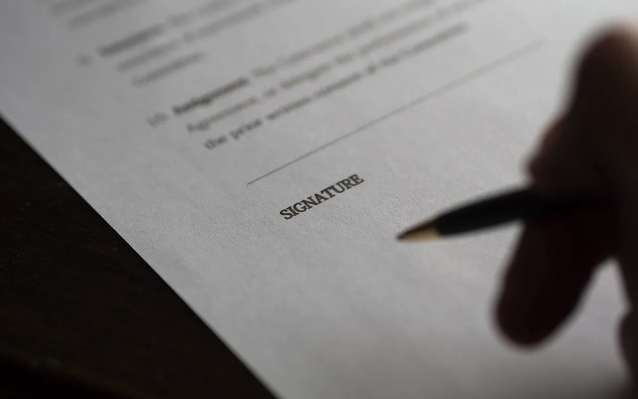 A contract page with a signature line, and a pen held just above it.