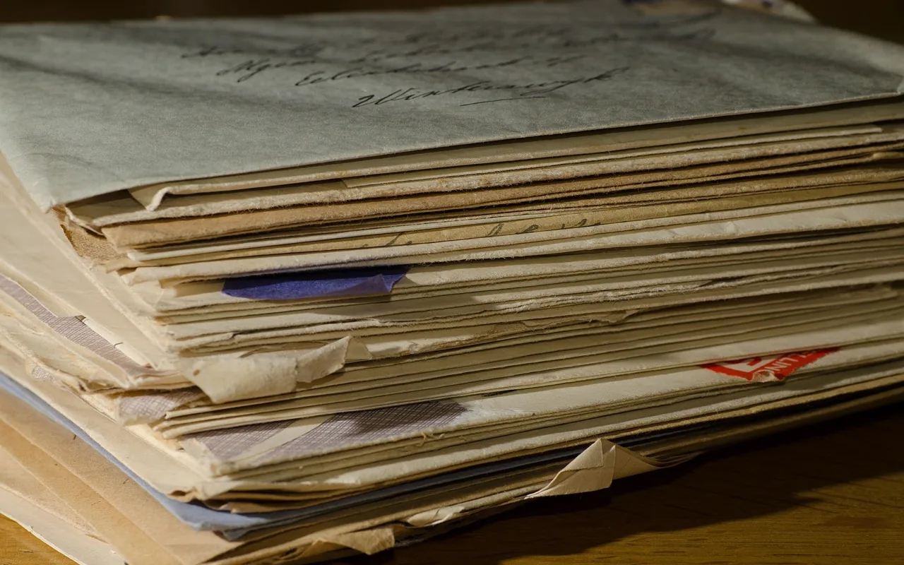 A thick stack of old letters and envelopes on a wood table.
