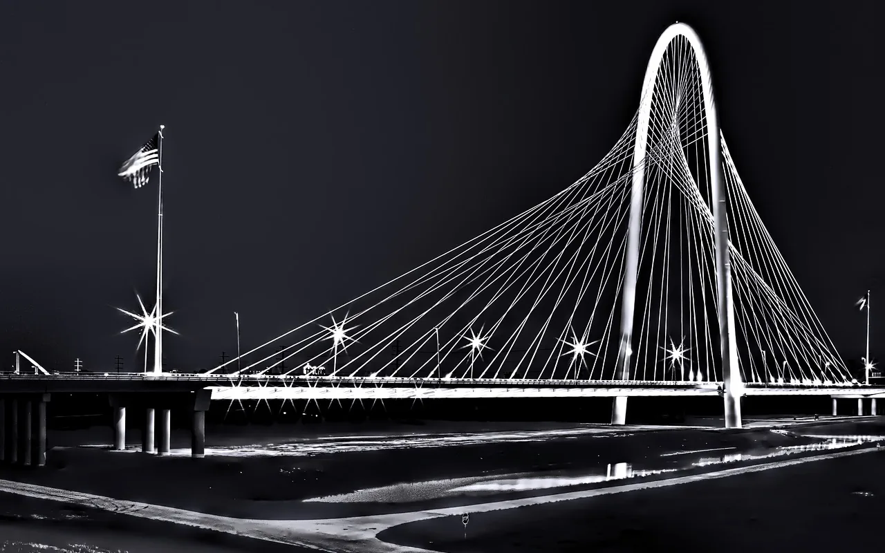 The white arch of the Margaret Hunt Hill Bridge over the Trinity in Dallas at night.