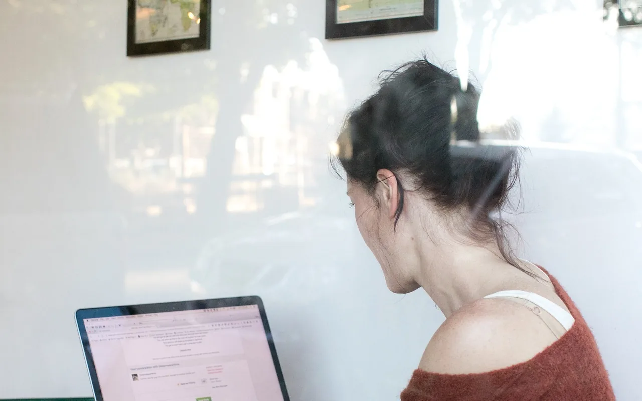 A person working at a laptop beside a bright window.