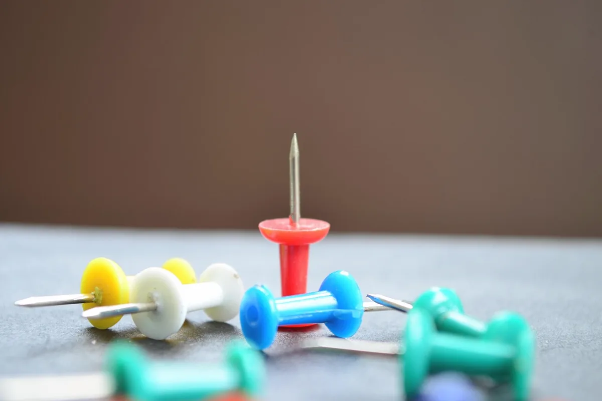 Colored push pins standing on a pale surface.
