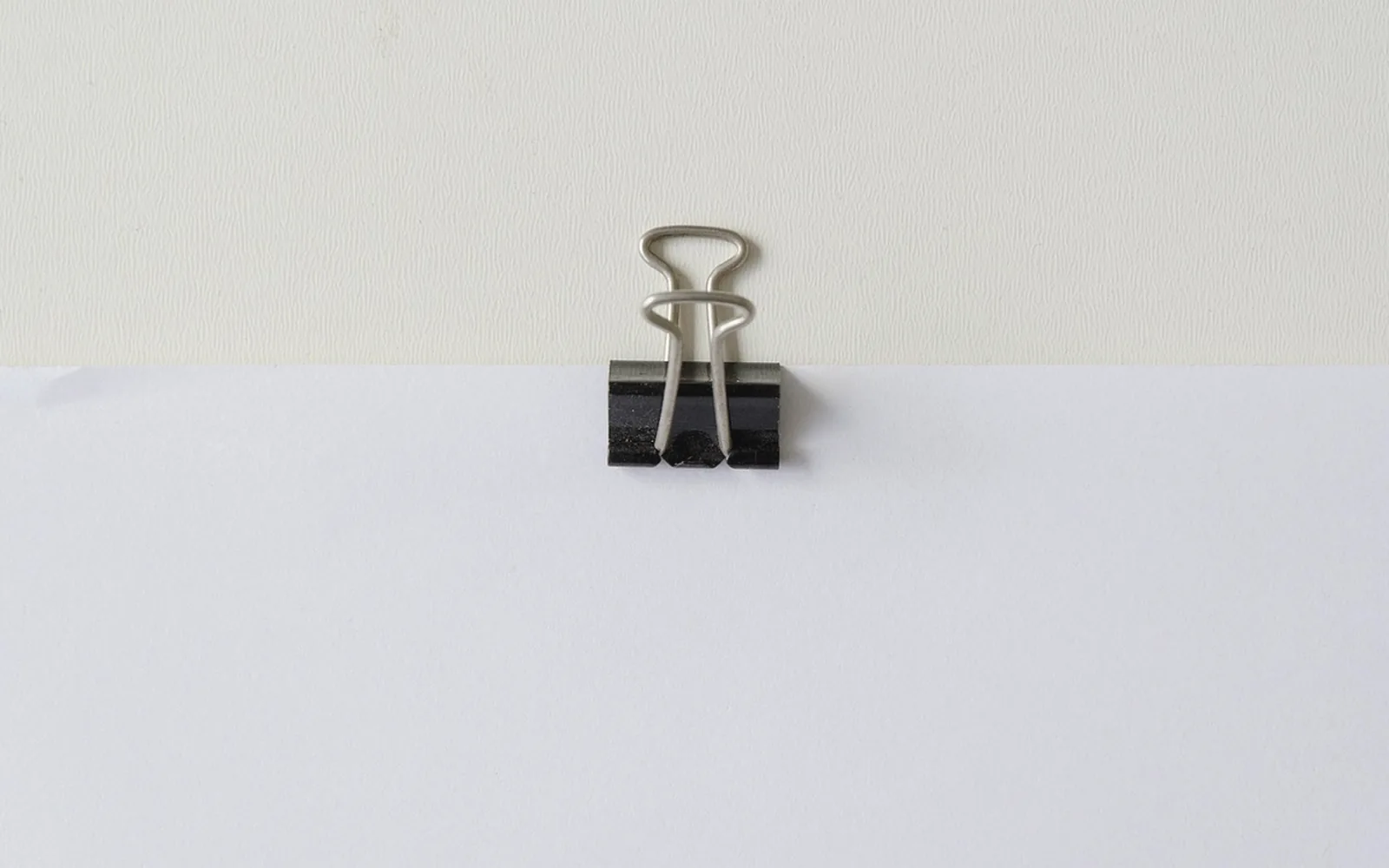 A single black binder clip on blank paper, with no writing.