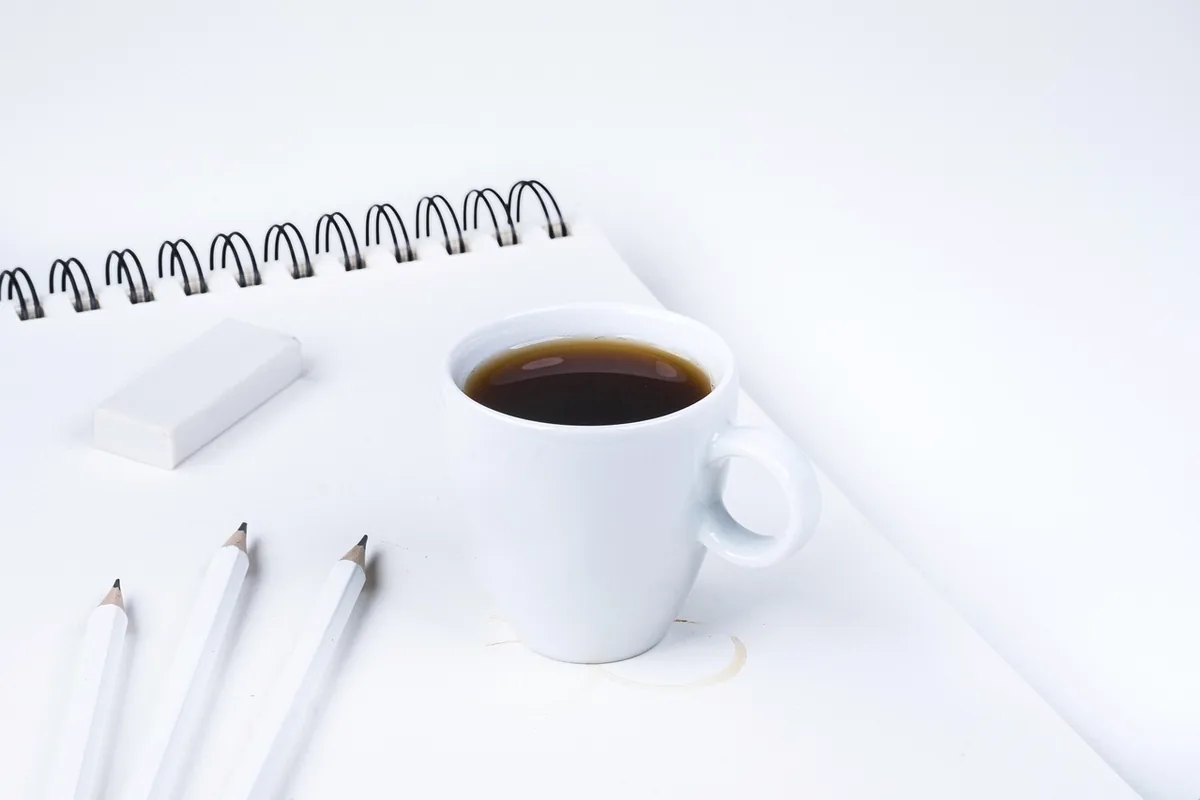 A notebook, a cup, and two pens, with no readable writing.