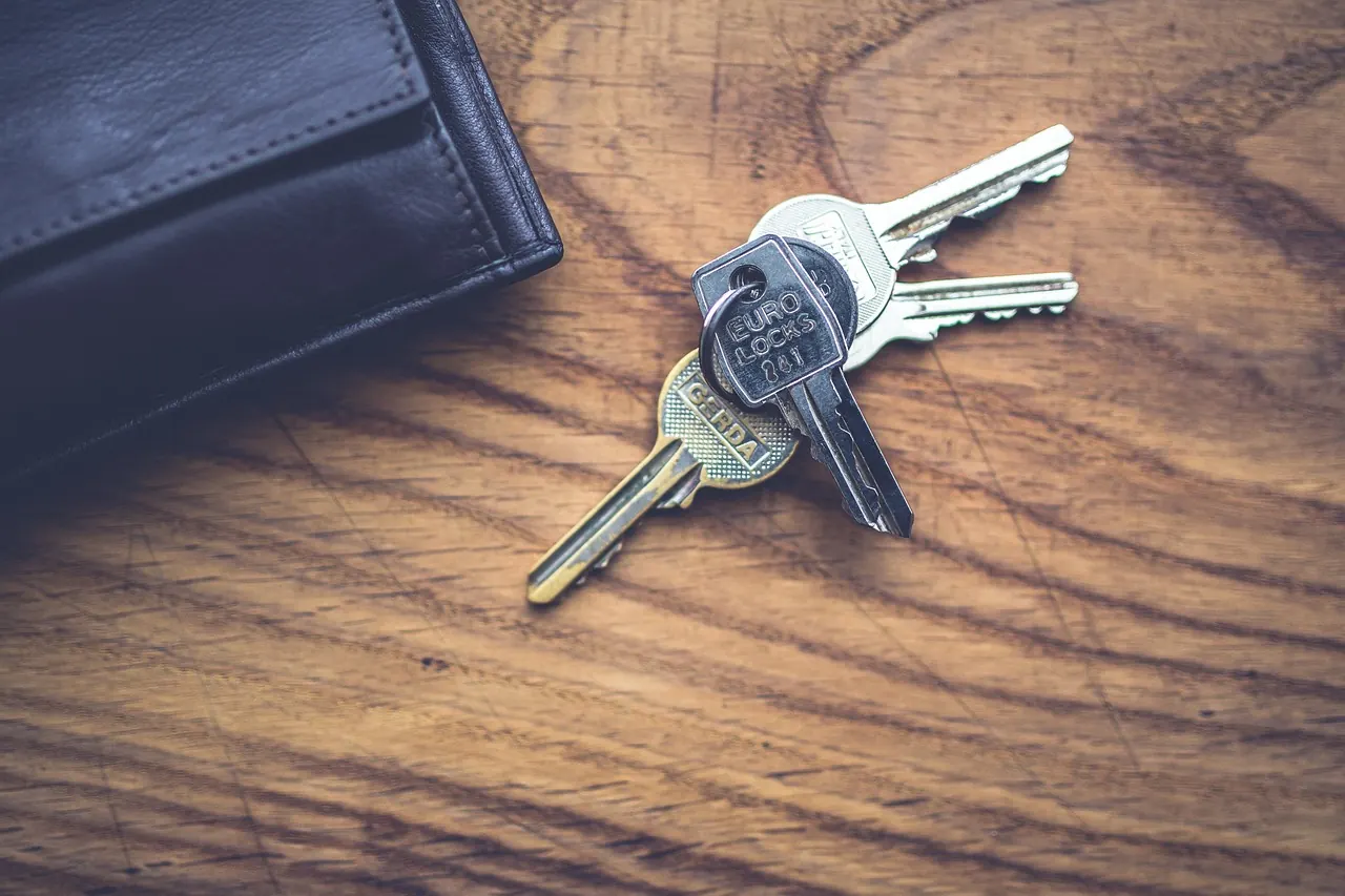 Several house keys on a ring beside a dark wallet, on a wooden table