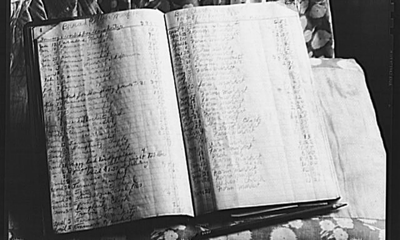 An open handwritten ledger with columns of figures, and a pen lying across the page.