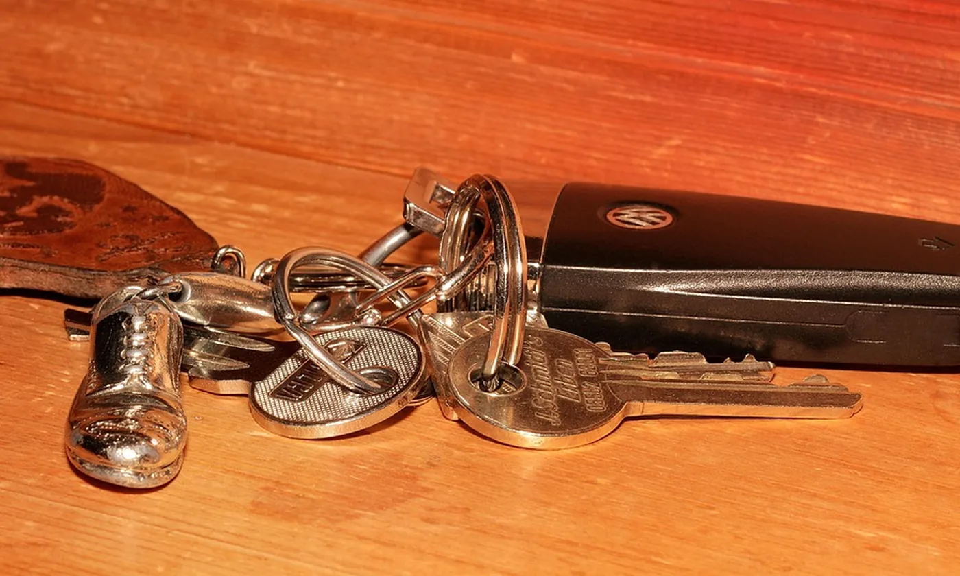 Keys, a small metal shoe charm, and a car fob resting on a wooden table.