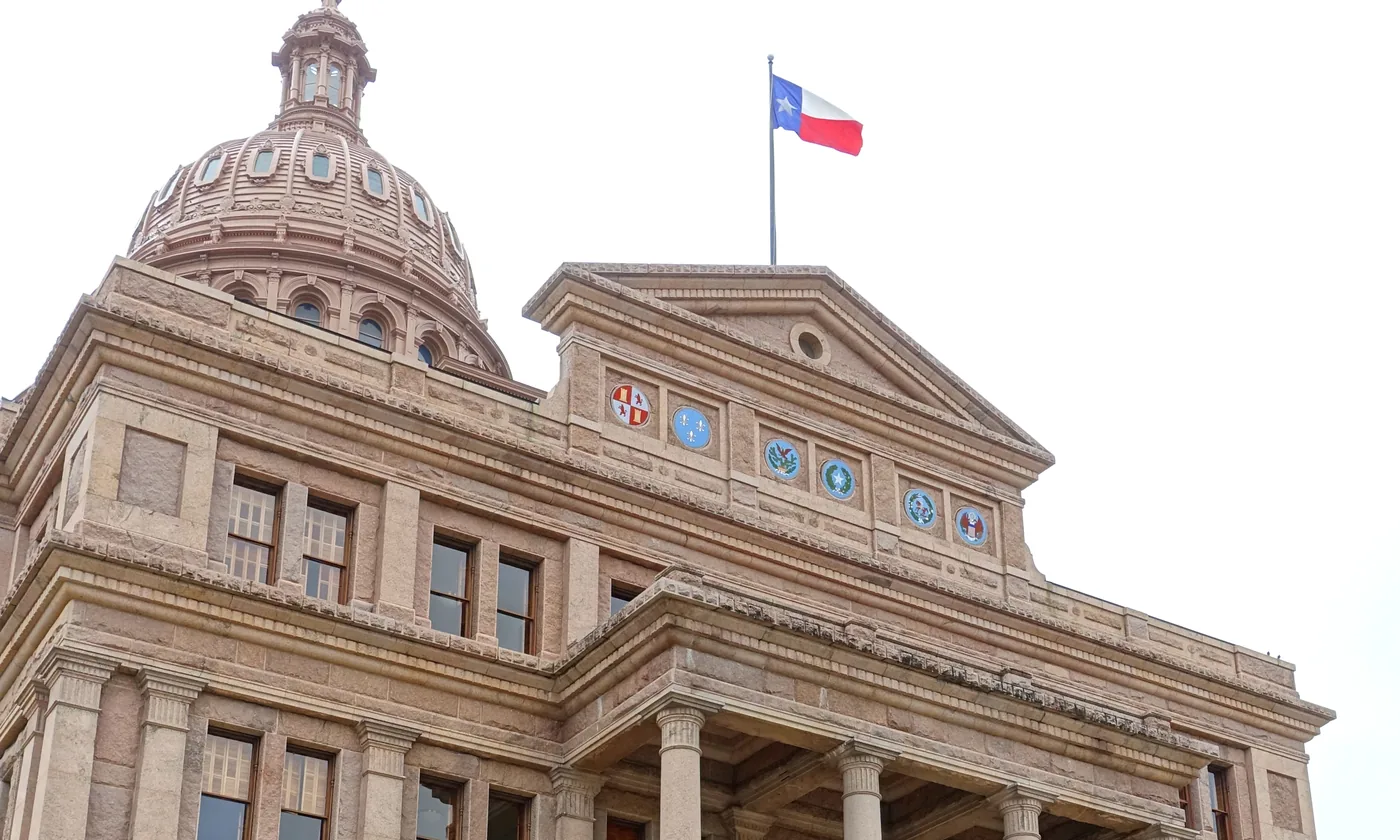 The Texas State Capitol in Austin, with the dome, the columns, and the state flag on the pole.