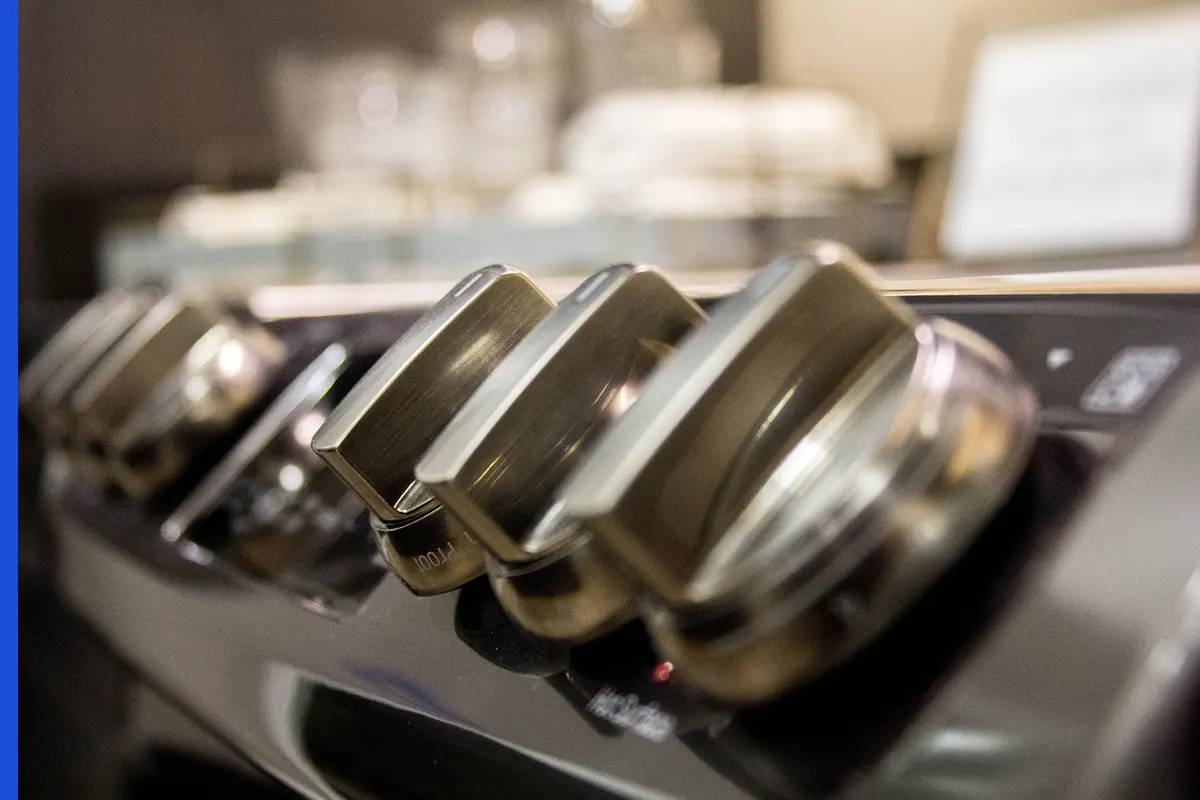 Metal stove knobs in a row, labels out of focus.