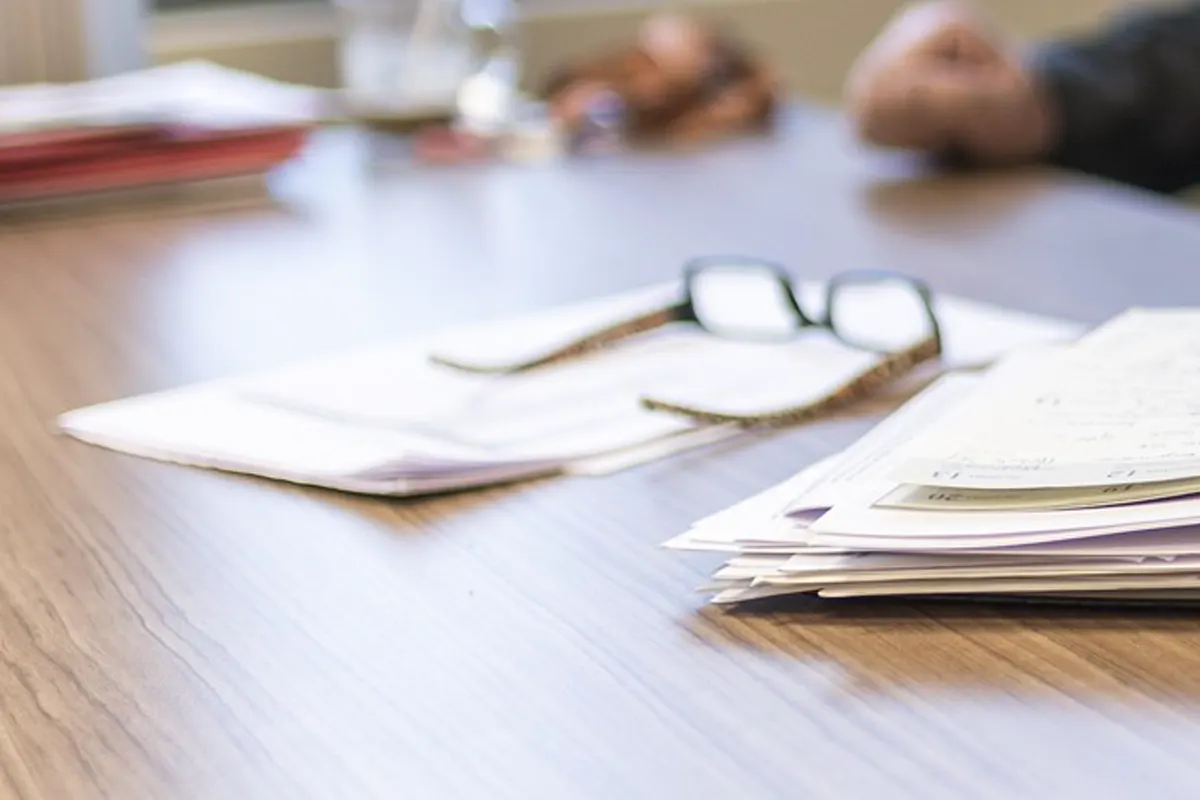 Glasses on a stack of papers at a wood table, no readable name.