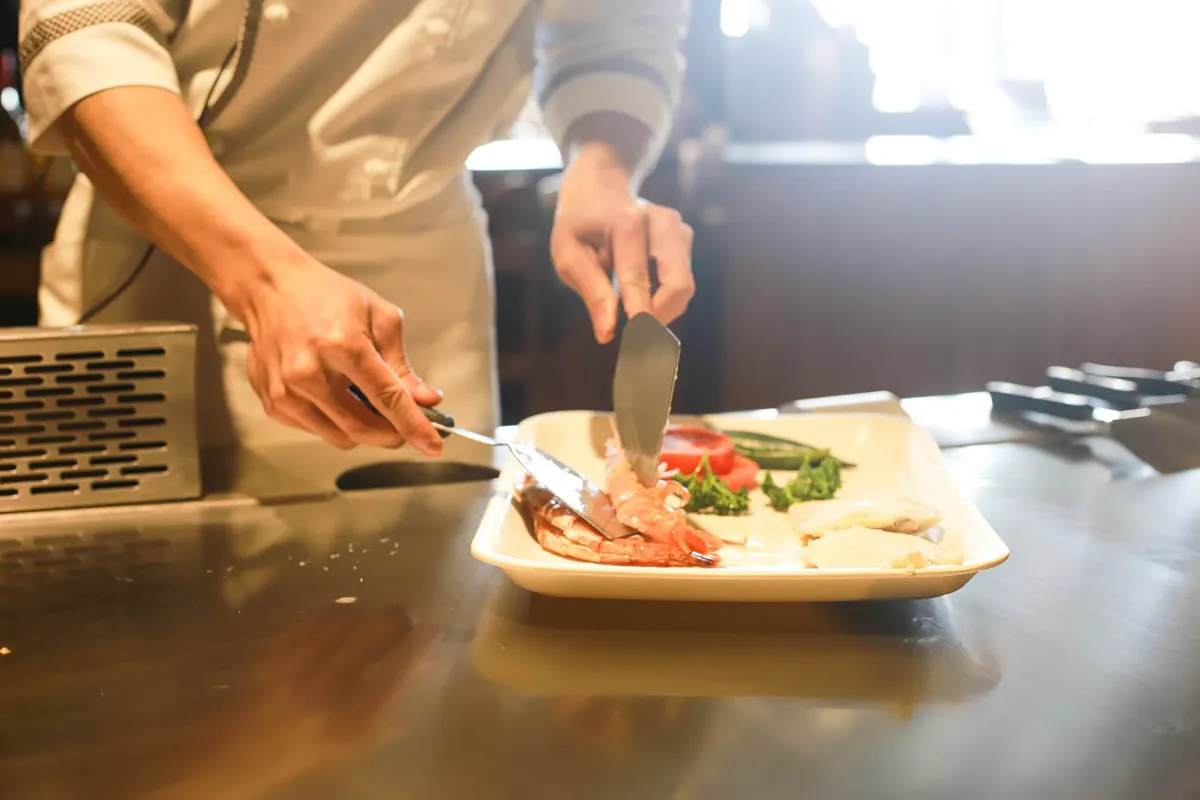 A cook plating shrimp on a steel line, face out of frame, no readable ticket.