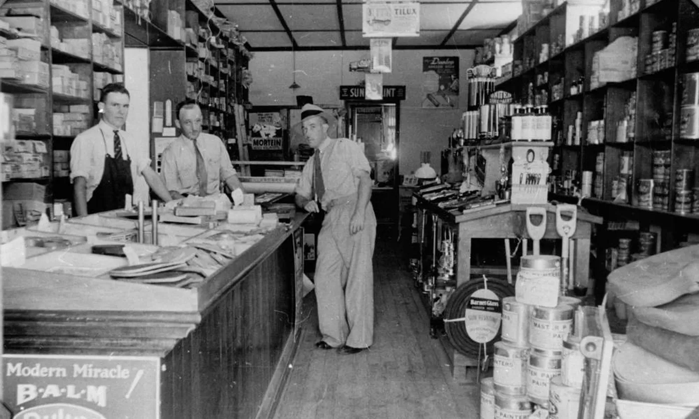 Three people at a hardware counter, with stock on the shelves behind them.