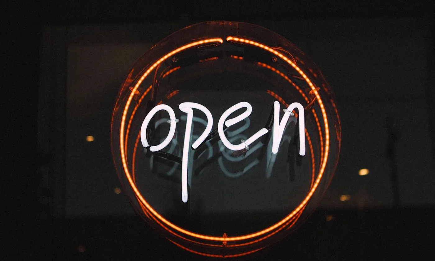 A round neon sign that says open, the door of a shop at night.