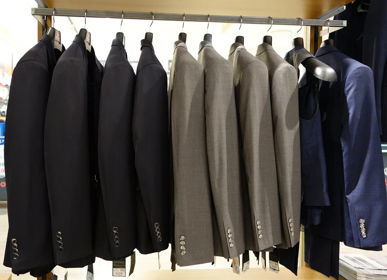 Suit jackets on a shop rail during the day, a floor that still has to match the file.