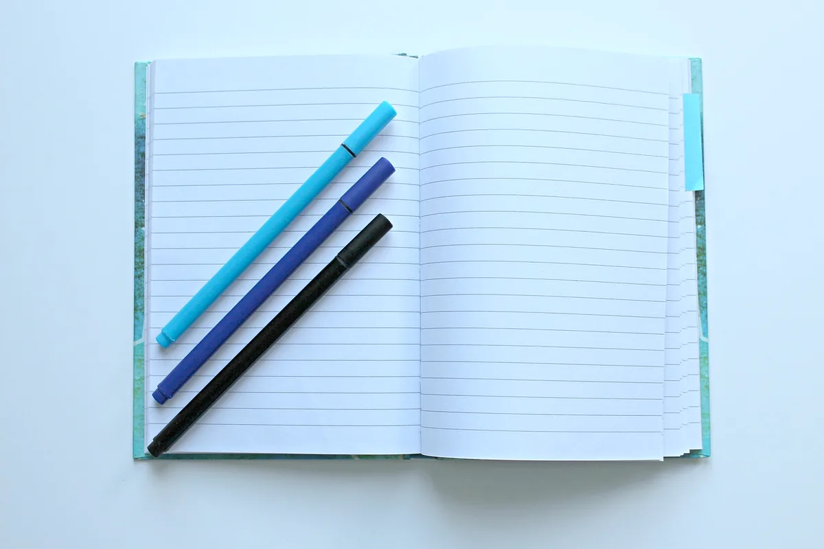 An open blank notebook with three pens on the left page.