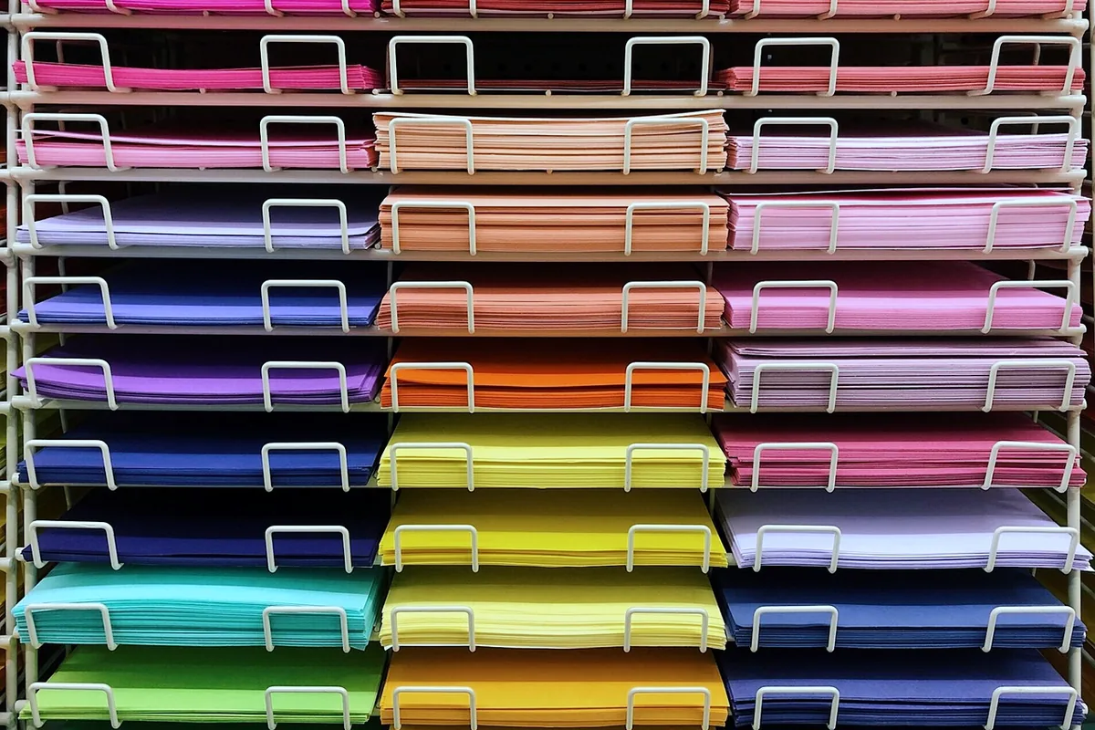 Stacks of colored paper in white racks.