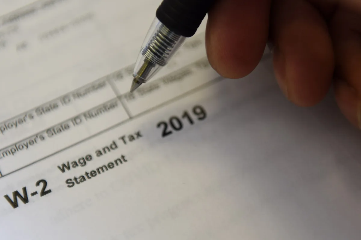 A hand holding a pen above a Wage and Tax Statement for 2019.