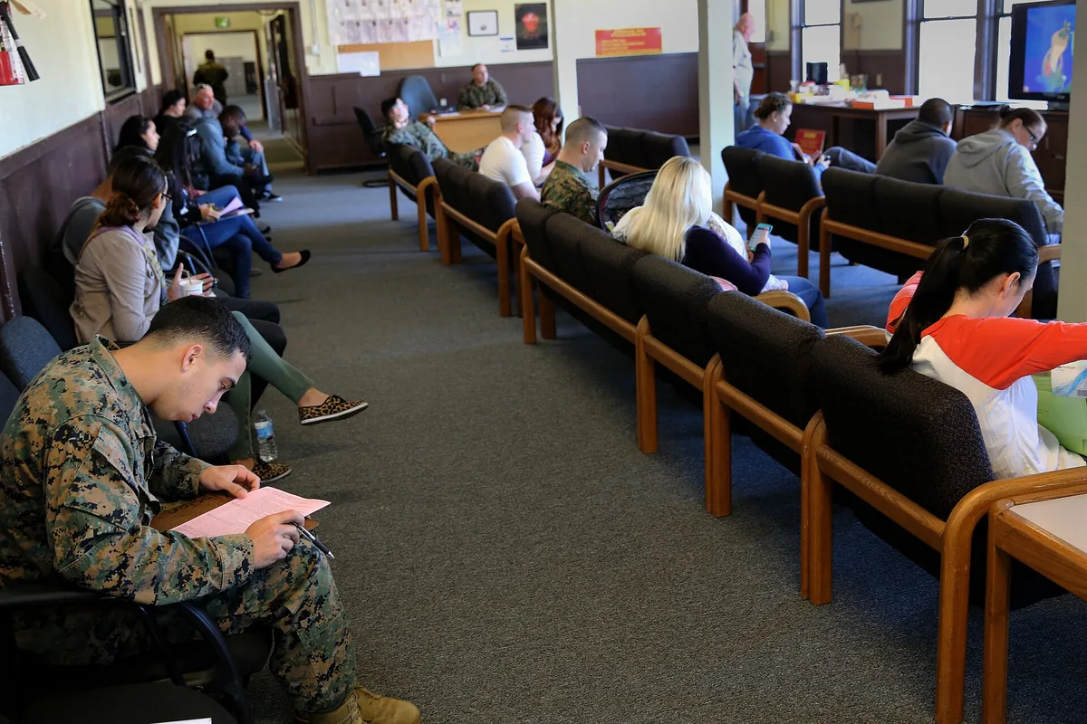 People in a waiting room holding papers, one person reading a page in the front row.