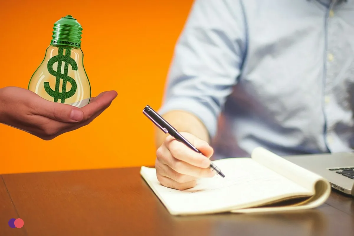 An owner writing in a notebook at a laptop while a hand holds out a dollar sign
