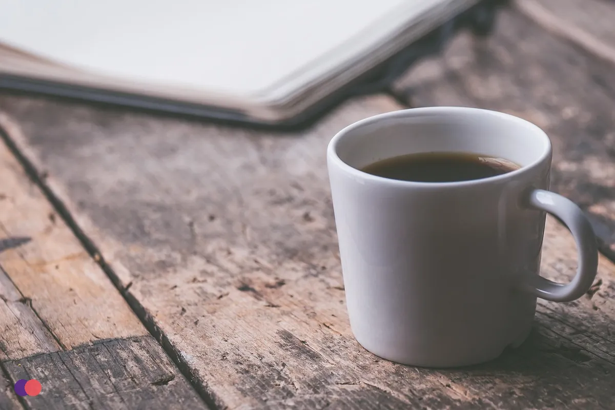 A mug of coffee beside a closed notebook on a wooden table