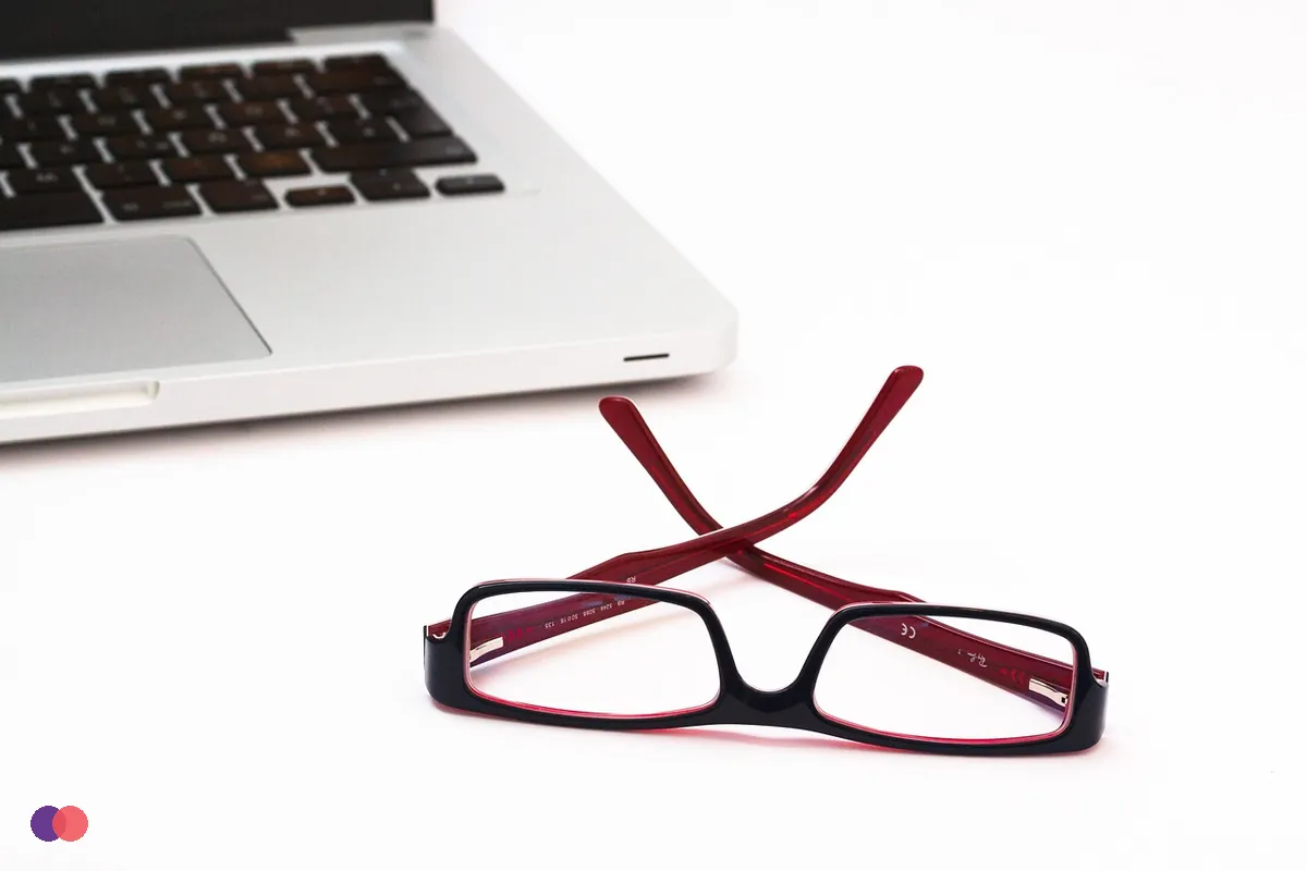 A pair of reading glasses beside a closed laptop on a white table