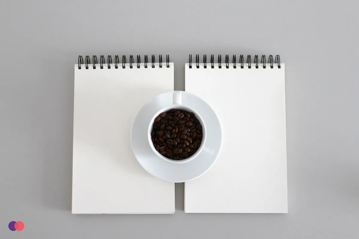 Two open notepads side by side with a cup of coffee between them
