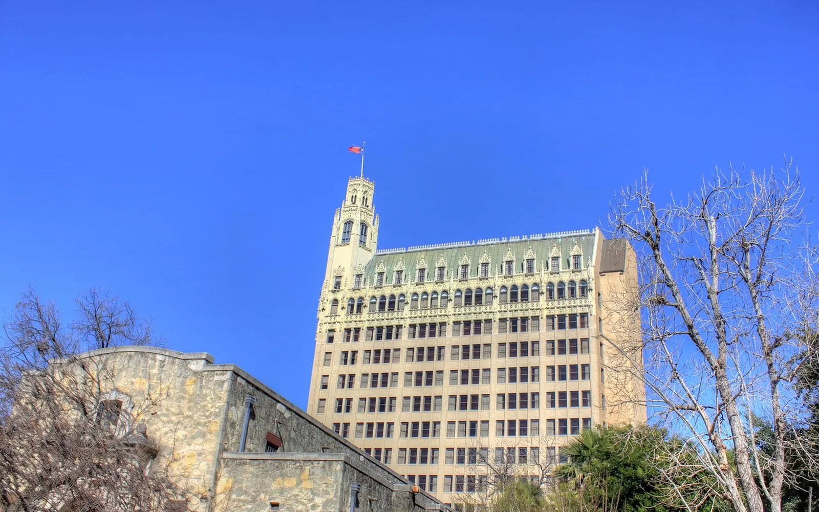 A San Antonio tower flying the Texas flag, with stone walls in the foreground.