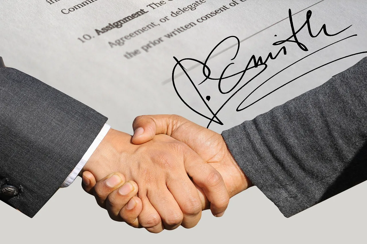 Two hands meet in a handshake over a printed assignment clause on the page