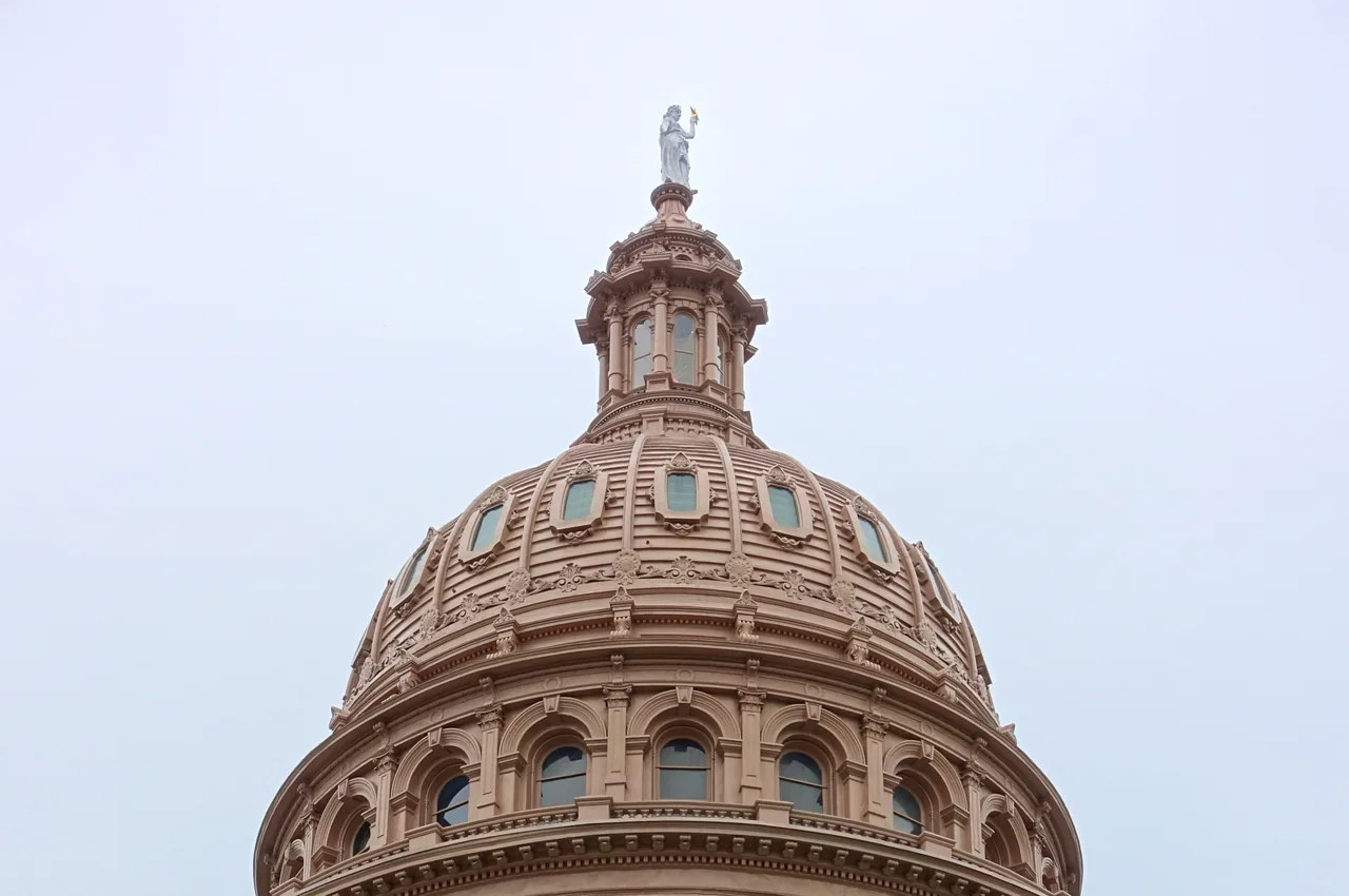 The pink granite dome of the Texas State Capitol and the star above it under a gray sky