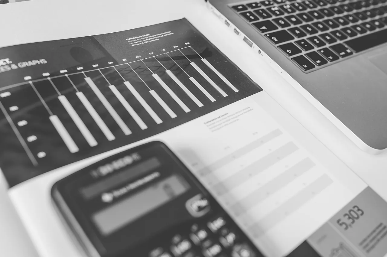 A calculator sits on a printed bar chart beside an open laptop