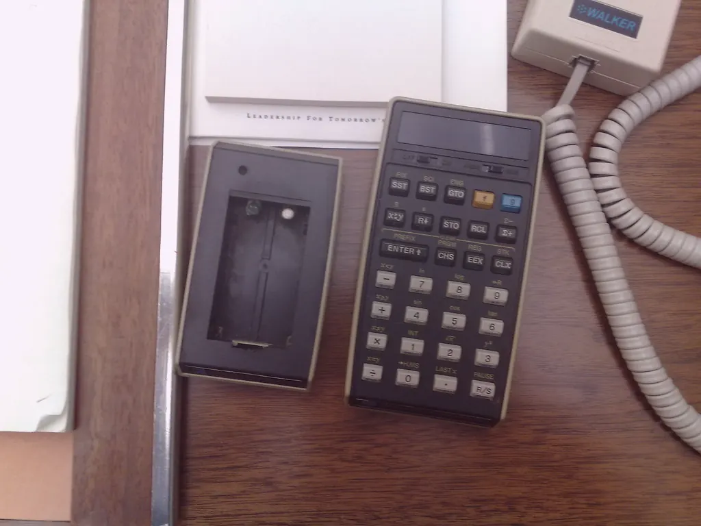 A handheld calculator lies beside a blank notepad and a coiled cord, ready for one number.