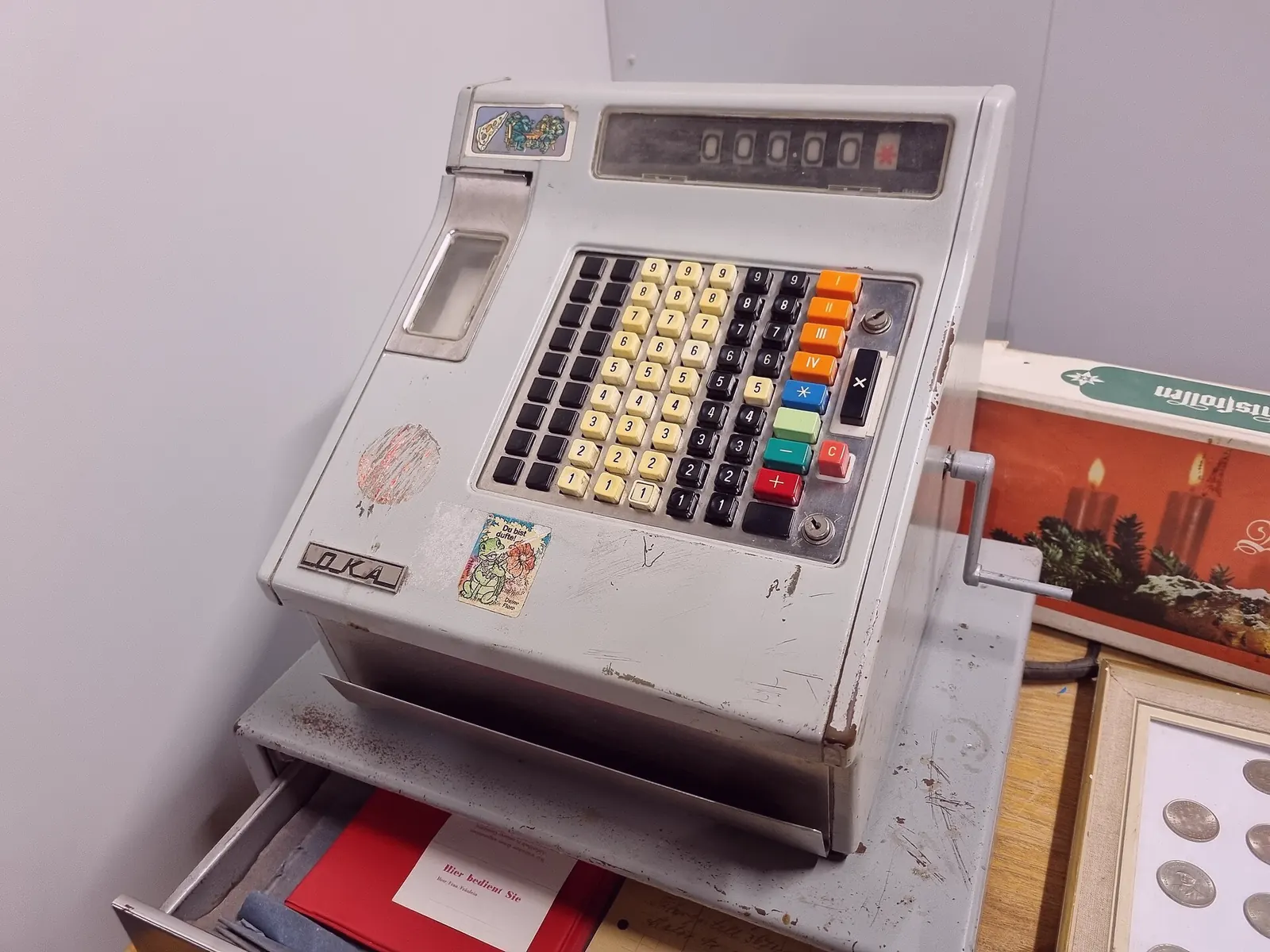 A gray cash register with a drawer of coins and a paper total reading zero.