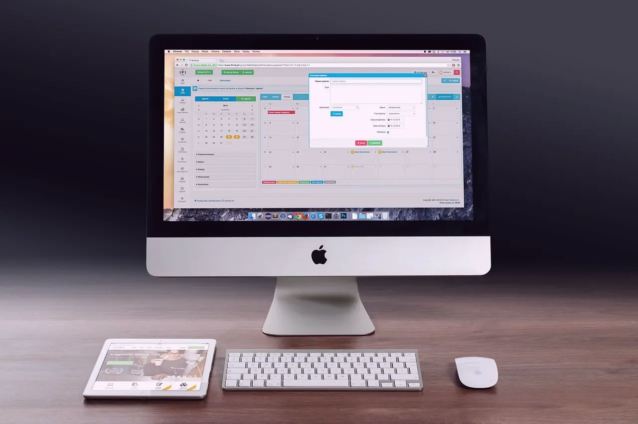 A computer screen shows a monthly calendar inside business software, with a keyboard and a tablet beside it.