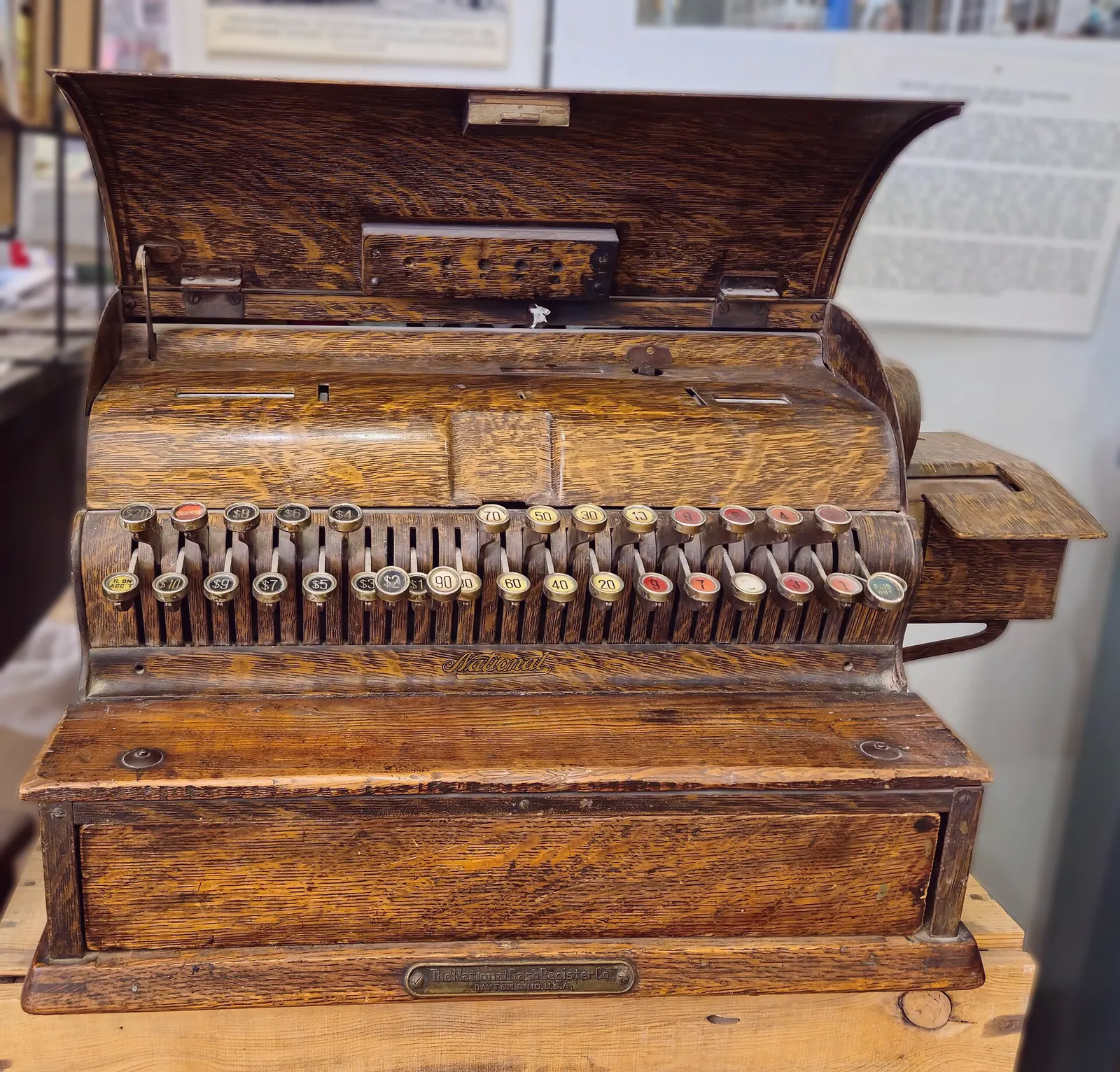 A wooden cash register stands open, with rows of amount keys and a closed drawer.